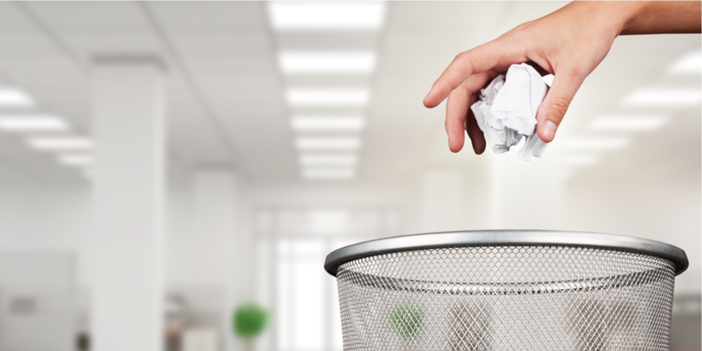 hand dropping crumpled paper into metal mesh wastebasket
